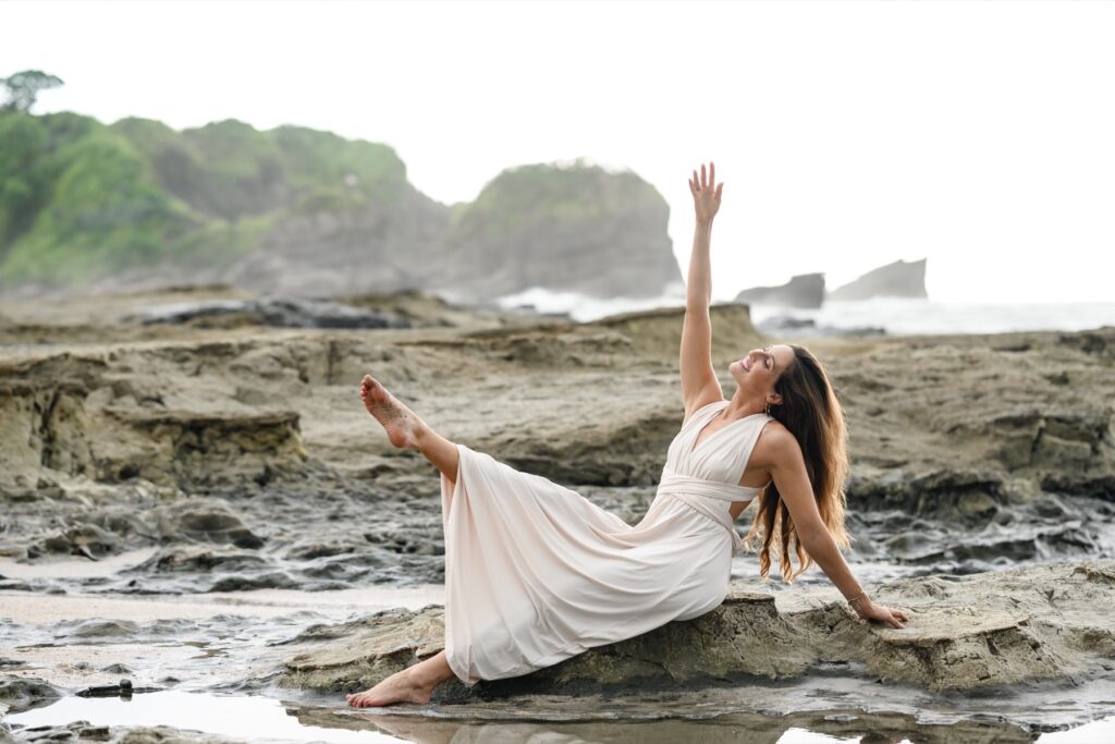 Hannah in a yoga pose on the rocks by the ocean